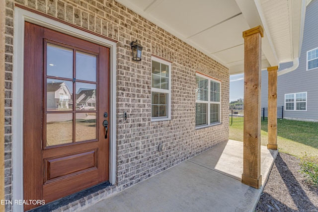 view of exterior entry featuring covered porch and brick siding