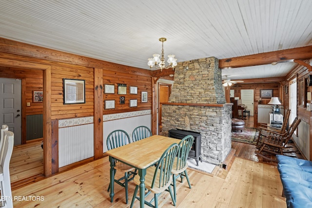 dining area featuring beamed ceiling, a stone fireplace, ceiling fan with notable chandelier, and light hardwood / wood-style floors