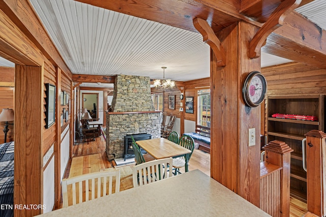 dining area featuring a stone fireplace, wood walls, an inviting chandelier, and light hardwood / wood-style flooring