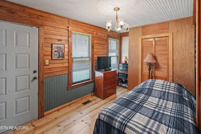 bedroom featuring wooden walls, a chandelier, light hardwood / wood-style floors, and a closet