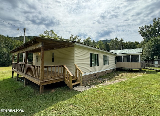 rear view of property featuring a sunroom, a yard, and a deck