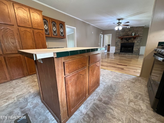 kitchen featuring crown molding, ceiling fan, a fireplace, a kitchen island, and stainless steel range with gas stovetop