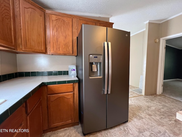 kitchen featuring tile countertops, stainless steel fridge, ornamental molding, and a textured ceiling