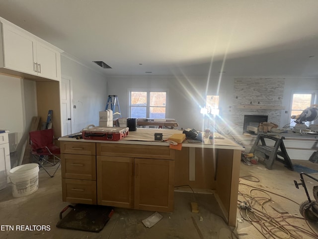 kitchen with a kitchen island, white cabinetry, crown molding, and a stone fireplace