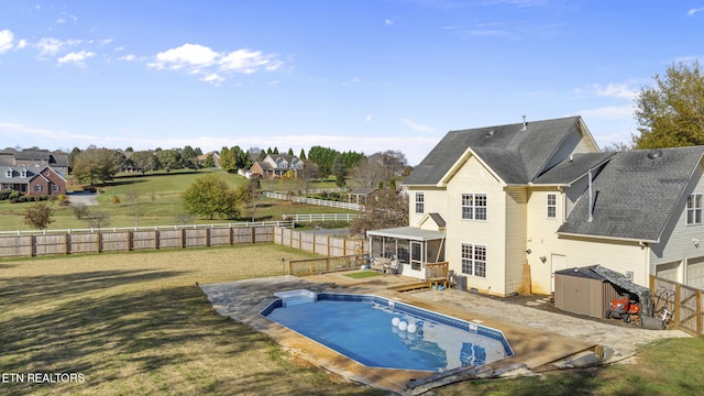 back of property featuring a shed, a sunroom, a fenced in pool, a patio, and a lawn