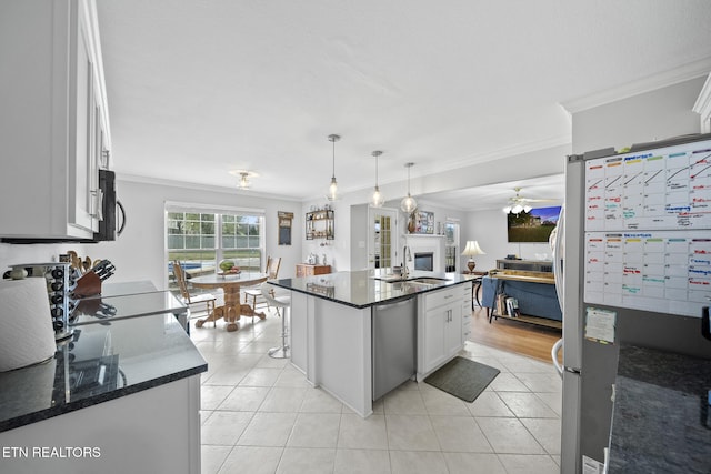 kitchen featuring stainless steel appliances, white cabinetry, a center island with sink, decorative light fixtures, and crown molding