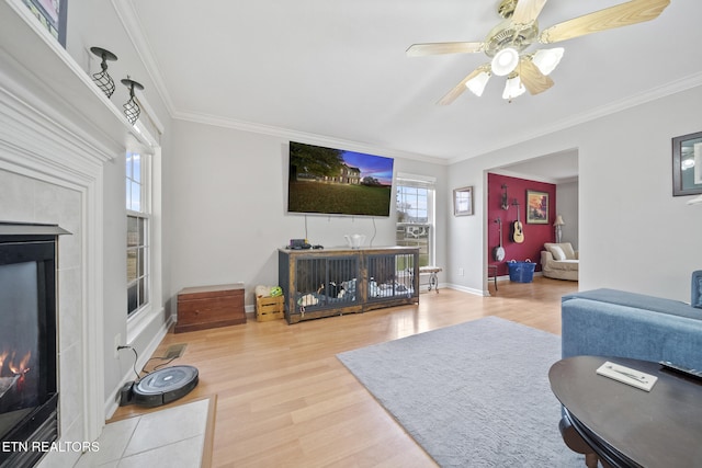 living room featuring a tiled fireplace, hardwood / wood-style flooring, ceiling fan, and crown molding