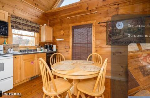 dining area featuring light hardwood / wood-style flooring, wooden walls, sink, and vaulted ceiling