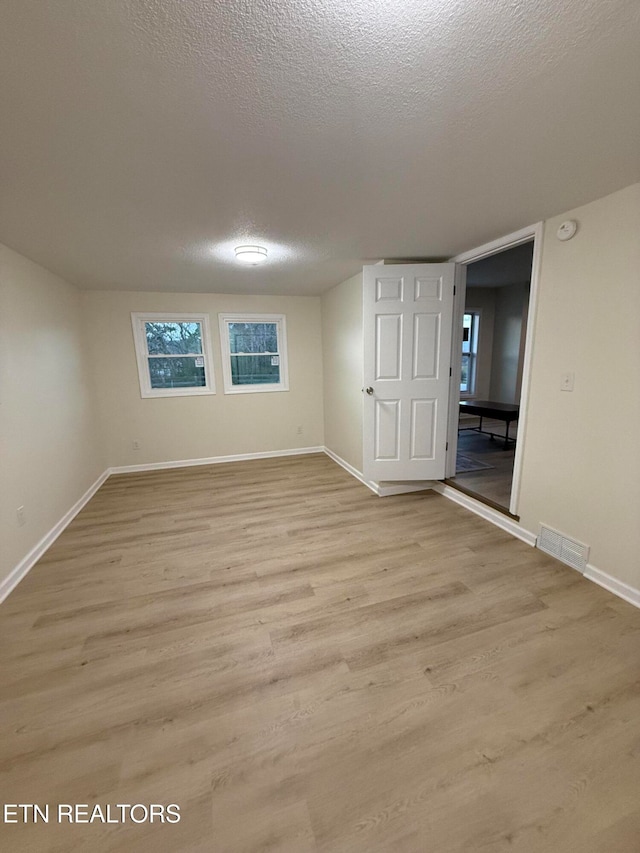 spare room featuring light wood-type flooring and a textured ceiling