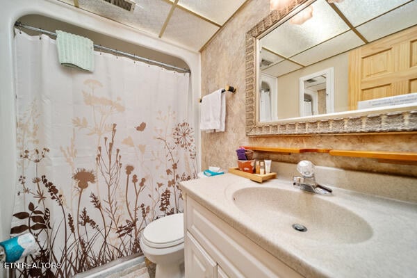 bathroom with a shower with curtain, a drop ceiling, vanity, and toilet