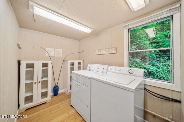 laundry room with washer and dryer, light wood-type flooring, and wooden walls