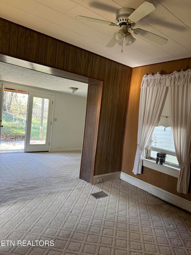 carpeted spare room with wood walls and ceiling fan