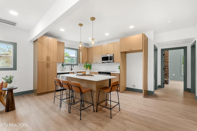 kitchen featuring stainless steel appliances, light wood-type flooring, light brown cabinets, hanging light fixtures, and a center island