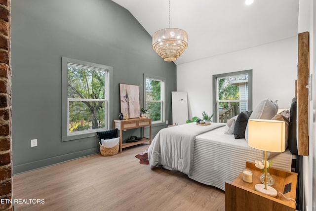 bedroom featuring an inviting chandelier, multiple windows, vaulted ceiling, and light hardwood / wood-style flooring