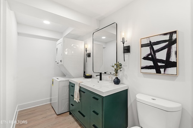 bathroom with hardwood / wood-style floors, vanity, toilet, and stacked washer / dryer