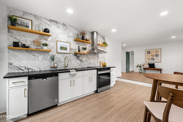 kitchen with stainless steel appliances, white cabinetry, sink, wall chimney range hood, and light wood-type flooring