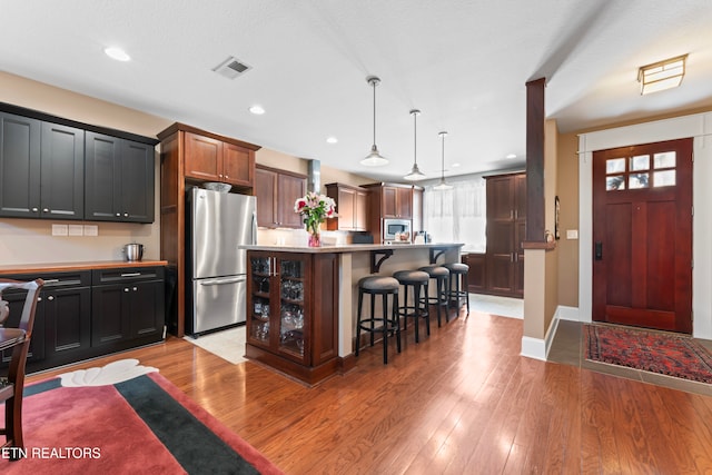 kitchen with appliances with stainless steel finishes, a kitchen breakfast bar, a center island, decorative light fixtures, and light wood-type flooring