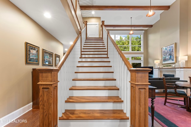 staircase featuring hardwood / wood-style flooring, a towering ceiling, and beam ceiling