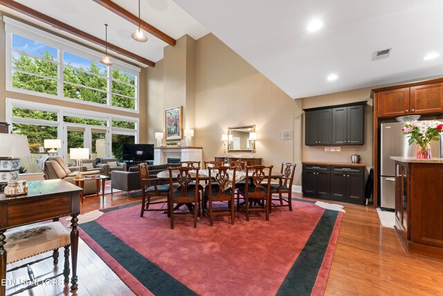 dining room with beamed ceiling, a high ceiling, and light wood-type flooring