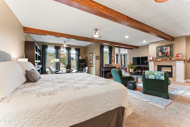 bedroom featuring a tiled fireplace, carpet floors, and beamed ceiling