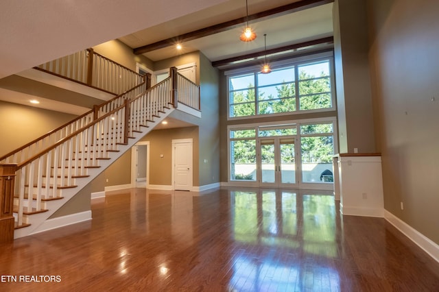 unfurnished living room with french doors, beamed ceiling, hardwood / wood-style floors, and a high ceiling