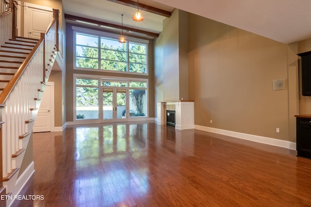 unfurnished living room featuring dark hardwood / wood-style floors, beam ceiling, and a towering ceiling