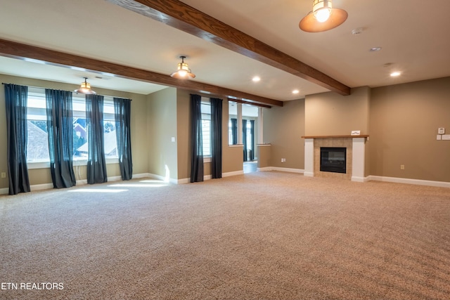 unfurnished living room featuring beamed ceiling, a tile fireplace, carpet, and a wealth of natural light