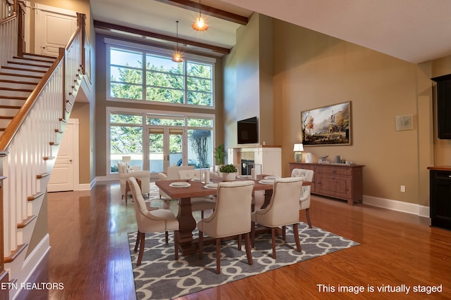 dining space featuring beamed ceiling, a towering ceiling, wood-type flooring, and a tile fireplace