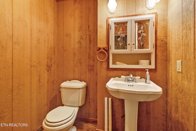 bathroom with hardwood / wood-style flooring, toilet, and wooden walls