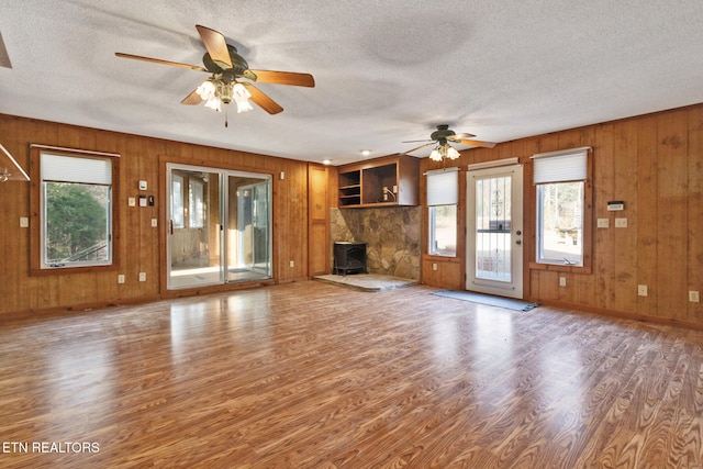 unfurnished living room featuring a textured ceiling, hardwood / wood-style flooring, ceiling fan, and wood walls