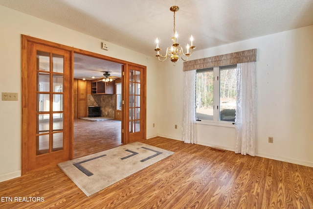 interior space with french doors, ceiling fan with notable chandelier, hardwood / wood-style flooring, a fireplace, and a textured ceiling