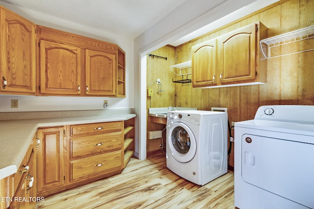 clothes washing area with light hardwood / wood-style floors, cabinets, and washing machine and dryer