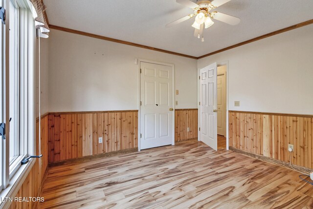 unfurnished room with crown molding, wooden walls, and light wood-type flooring