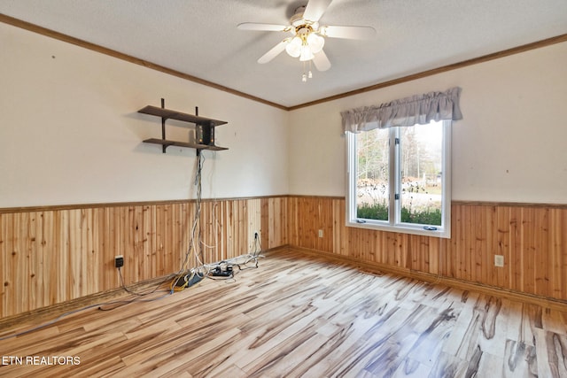 unfurnished room with ornamental molding, a textured ceiling, light hardwood / wood-style flooring, and wooden walls