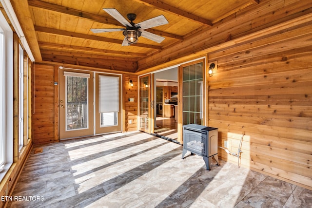 unfurnished sunroom with beam ceiling, a wood stove, ceiling fan, and wooden ceiling