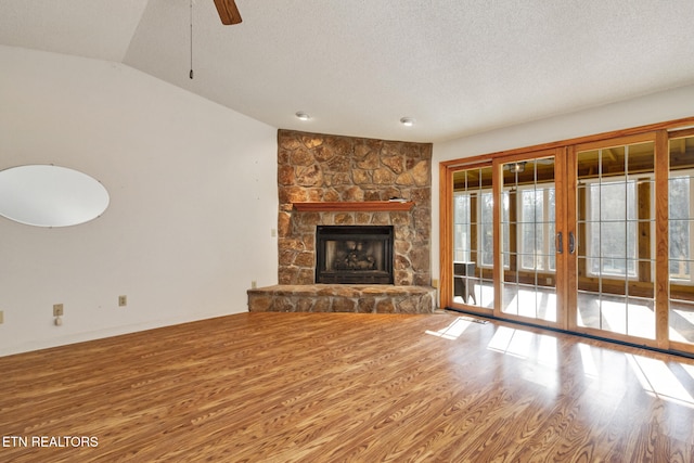 unfurnished living room with lofted ceiling, ceiling fan, a textured ceiling, a fireplace, and wood-type flooring