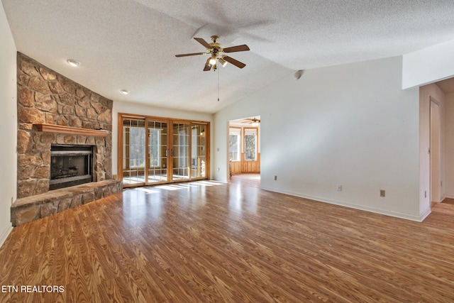 unfurnished living room with a stone fireplace, vaulted ceiling, ceiling fan, a textured ceiling, and light hardwood / wood-style floors