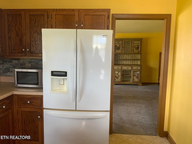 kitchen featuring white fridge with ice dispenser, decorative backsplash, and light tile patterned floors