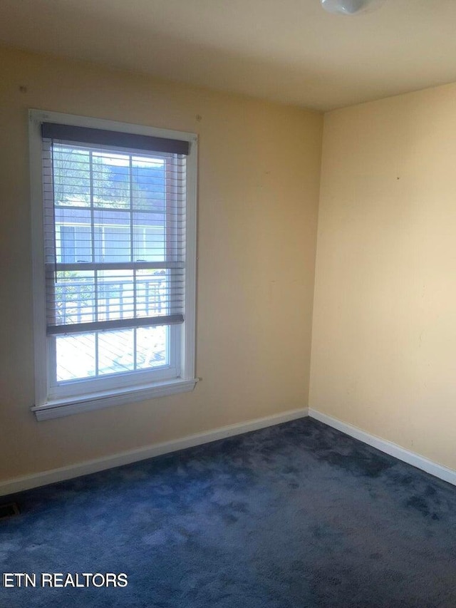 unfurnished room with a healthy amount of sunlight and dark colored carpet