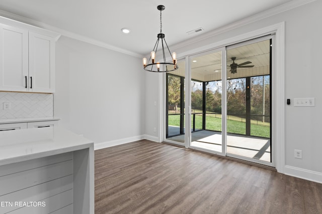 unfurnished dining area featuring dark wood-type flooring, ornamental molding, and ceiling fan with notable chandelier