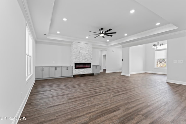 unfurnished living room with a stone fireplace, a tray ceiling, ornamental molding, and dark hardwood / wood-style floors