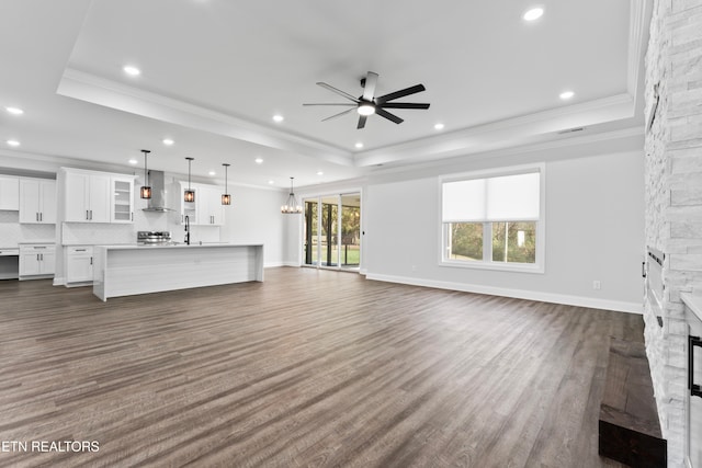 unfurnished living room with a fireplace, crown molding, dark hardwood / wood-style floors, a raised ceiling, and ceiling fan with notable chandelier