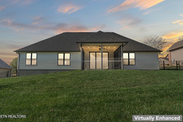 back house at dusk featuring a lawn