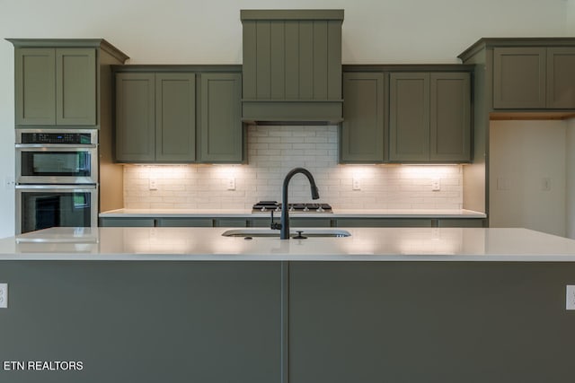 kitchen with stainless steel appliances, green cabinets, sink, and backsplash