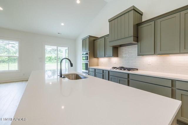 kitchen featuring light hardwood / wood-style floors, stainless steel appliances, vaulted ceiling, sink, and backsplash