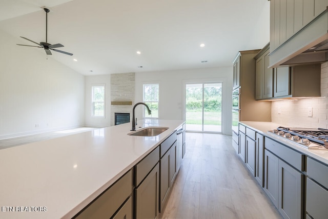 kitchen featuring stainless steel gas stovetop, decorative backsplash, sink, a fireplace, and light hardwood / wood-style flooring