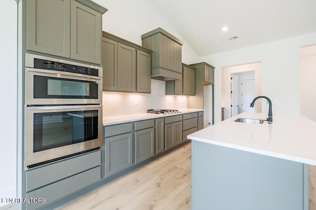 kitchen with stainless steel appliances, light wood-type flooring, decorative backsplash, sink, and lofted ceiling