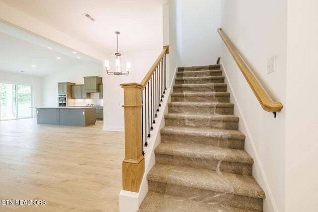 stairway with hardwood / wood-style floors, lofted ceiling, and a notable chandelier