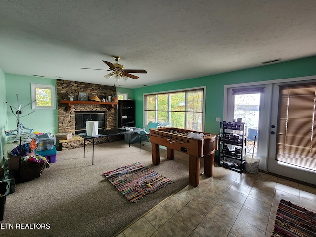 recreation room with a textured ceiling, carpet flooring, ceiling fan, and a fireplace