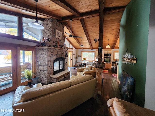 living room with hardwood / wood-style floors, ceiling fan, beamed ceiling, and a stone fireplace